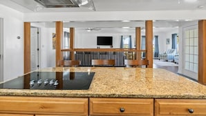 A kitchen with granite countertops, a black induction cooktop, wooden cabinets, and a ceiling fan. - Corpus Christi Gem (Corpus Christi)