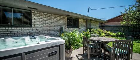 A backyard with a hot tub, a wooden table, and chairs.