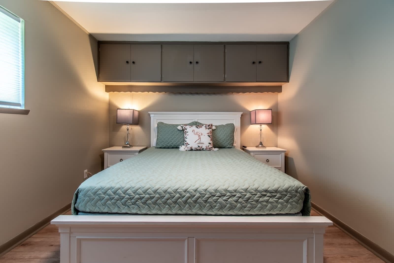 A bedroom with a bed, two bedside tables, a nightstand, a window, and a built-in cabinet above the bed.