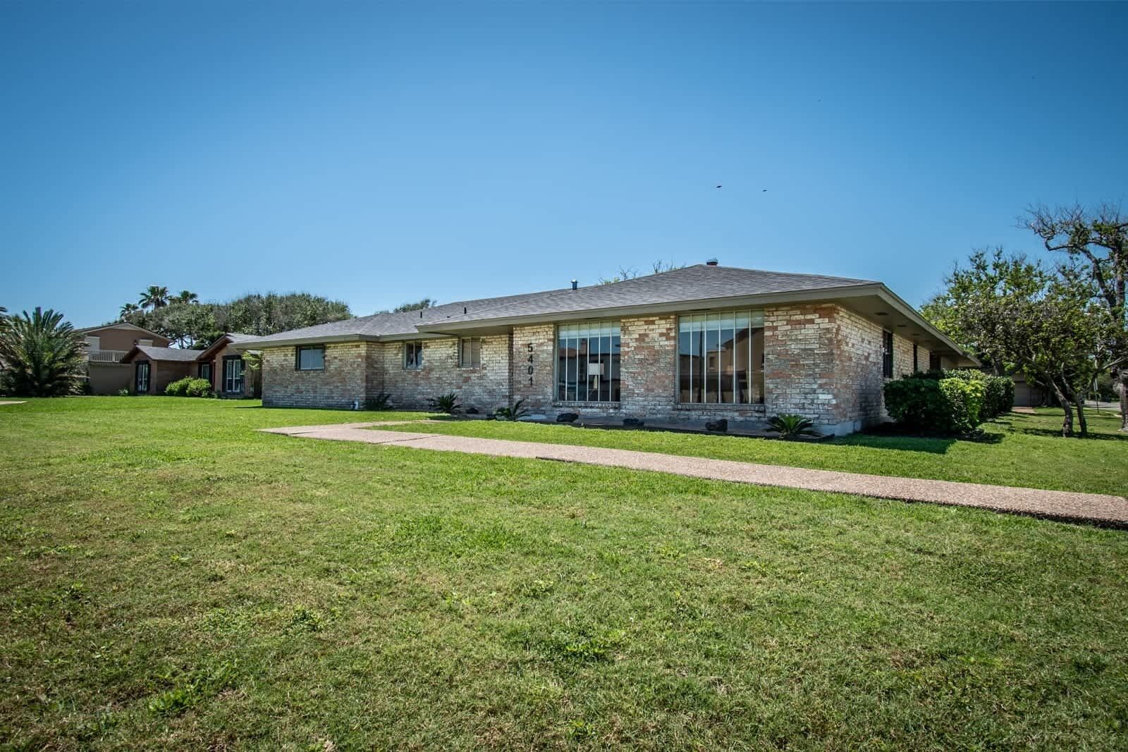A single-story brick house with a front porch, a driveway, and a well-maintained lawn.