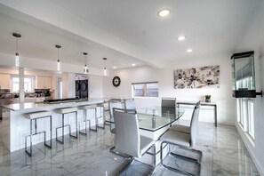 A modern kitchen with a central island, bar stools, and a dining table with chairs.