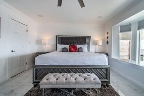 A bedroom with a large bed, a bench, and a view of the outside.