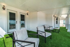 A covered outdoor area with artificial grass, white chairs, and tables. - Ocean Drive Splendor Awaits (Corpus Christi)