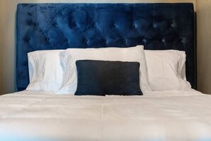 A bed with a tufted headboard, white bedding, and a dark pillow. - Ocean Drive Oasis w Hot Tub Awaits (Corpus Christi)
