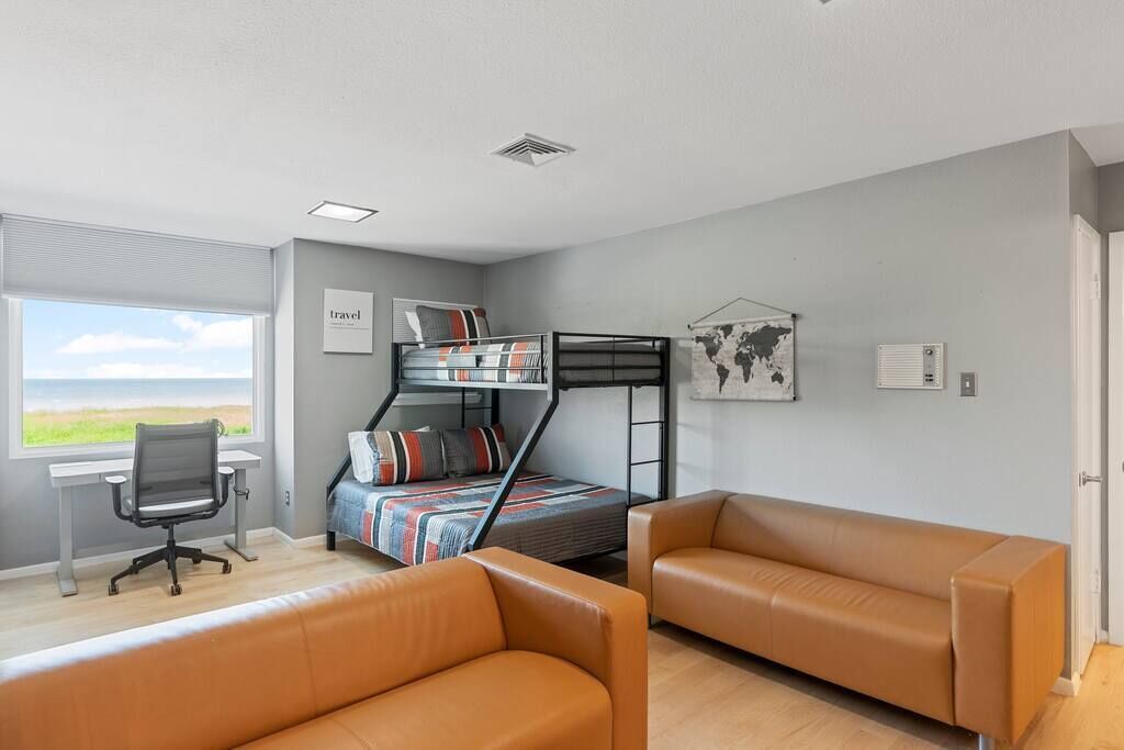 Een moderne kamer met een stapelbed, een bureau, twee leren sofa’s, een groot raam en een wereldkaart aan de muur.