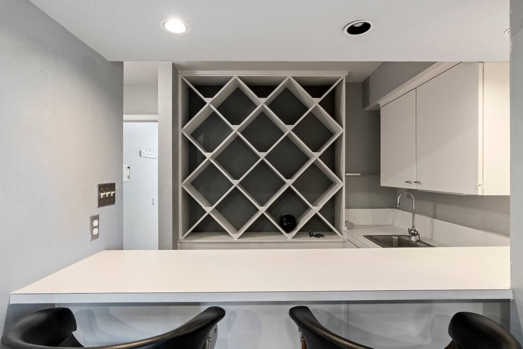 Una cocina moderna con encimera blanca, un armario para vinos empotrado y un lavamanos.