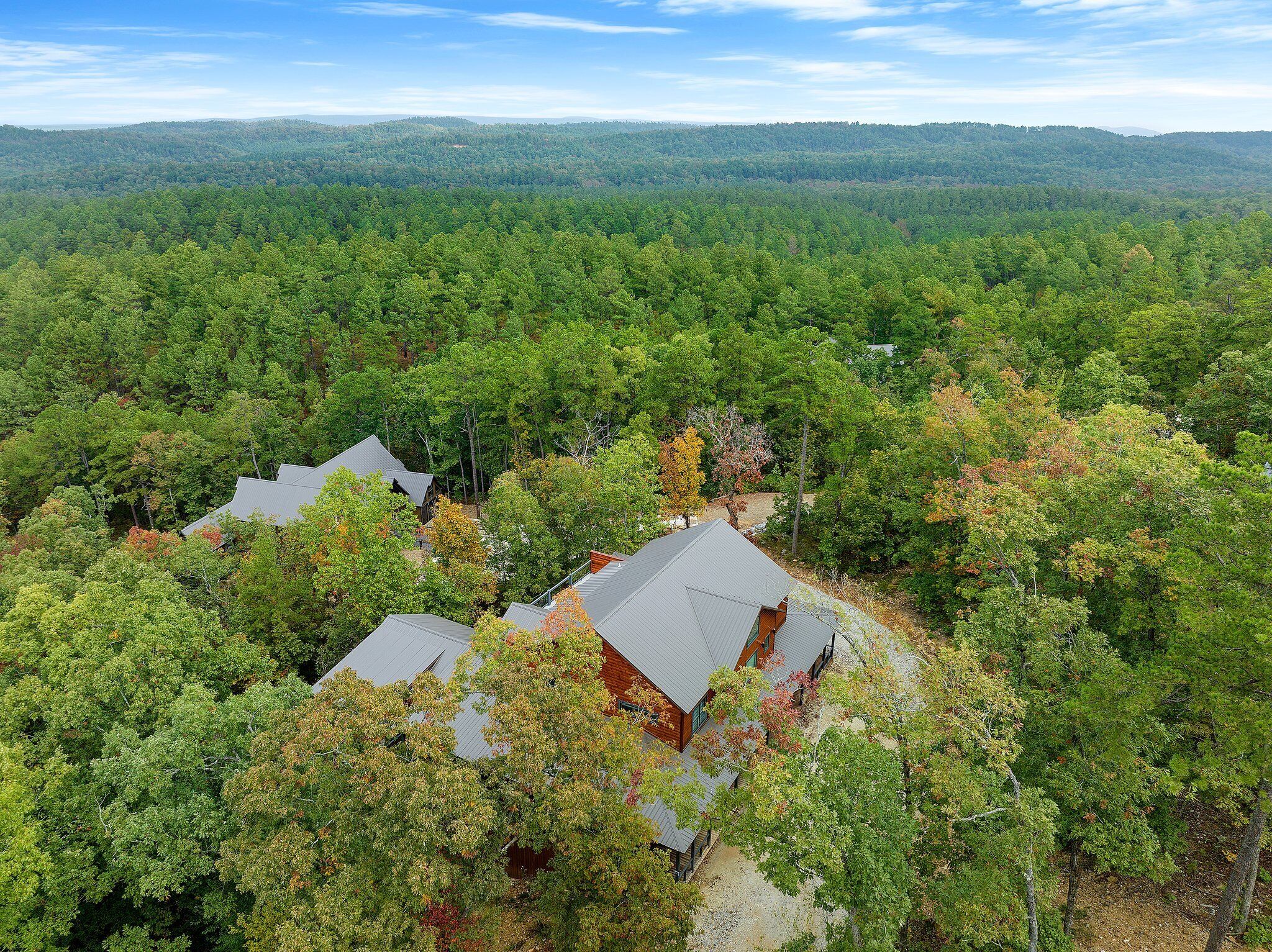 A residential area with multiple houses surrounded by dense forest, with a clear view of the surrounding hills.