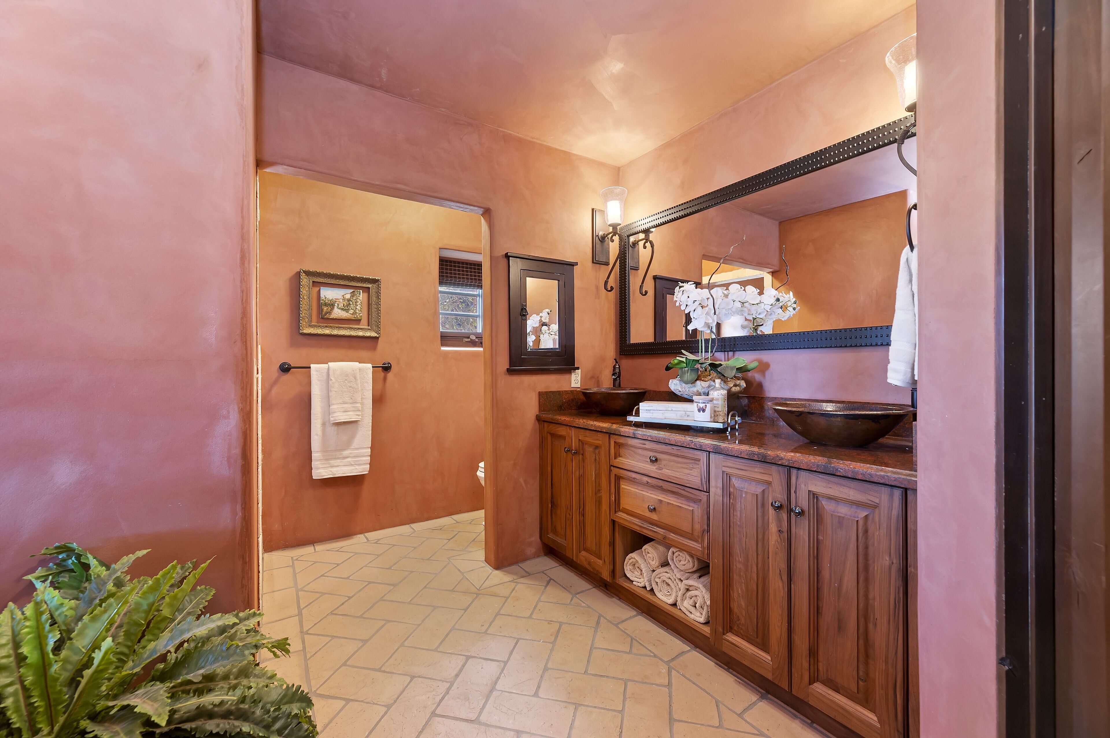 A bathroom with wooden cabinets, a large mirror, a sink with a bowl, and a potted orchid.