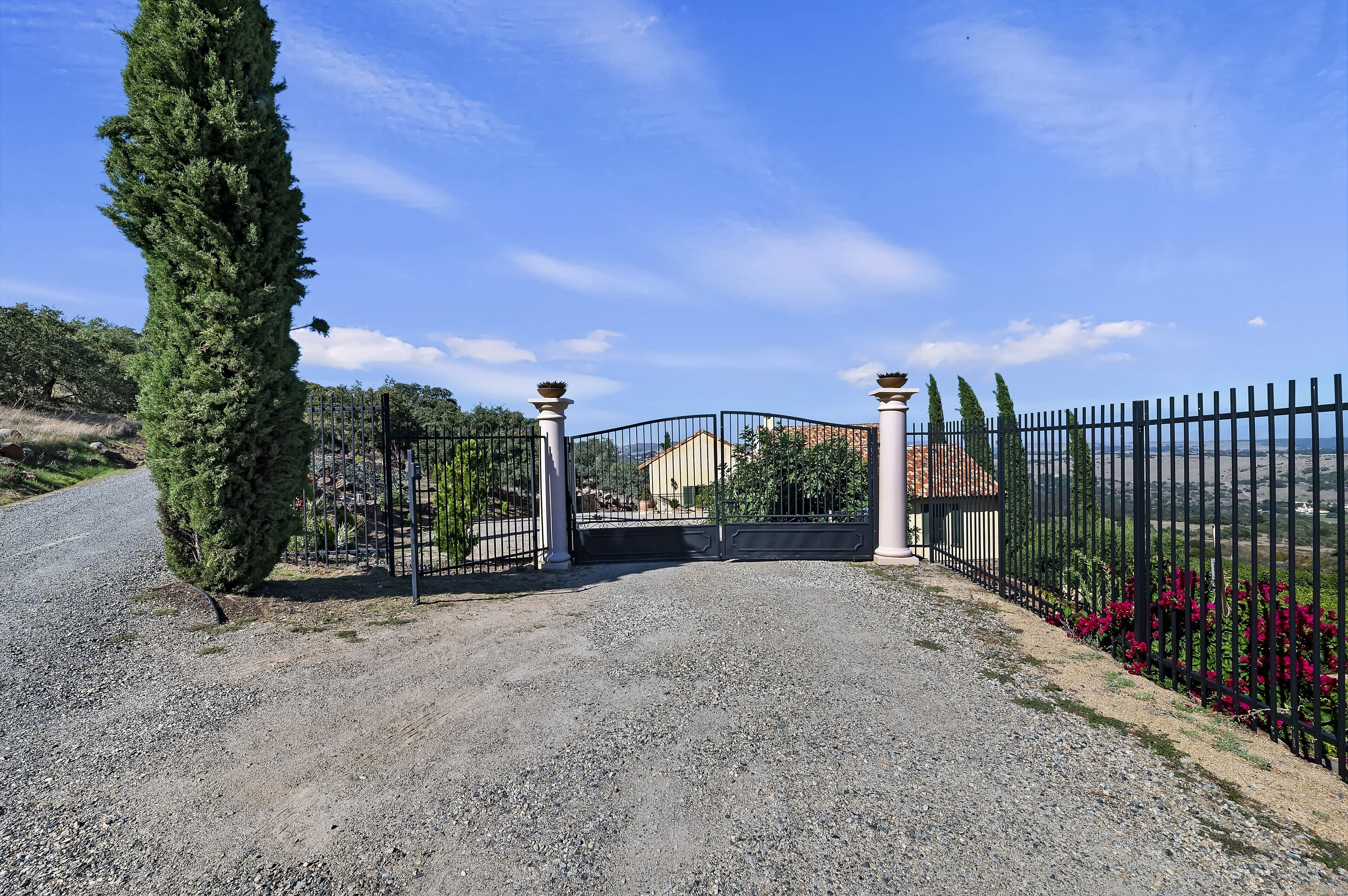 A gravel driveway leading to a gated entrance with a house in the background.