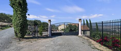 A gravel driveway leading to a gated entrance with a house in the background.