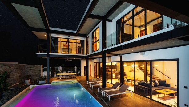 Ett modernt hus med flera våningar, en swimmingpool, en uteplats och en trappa som leder upp till de övre våningarna.
