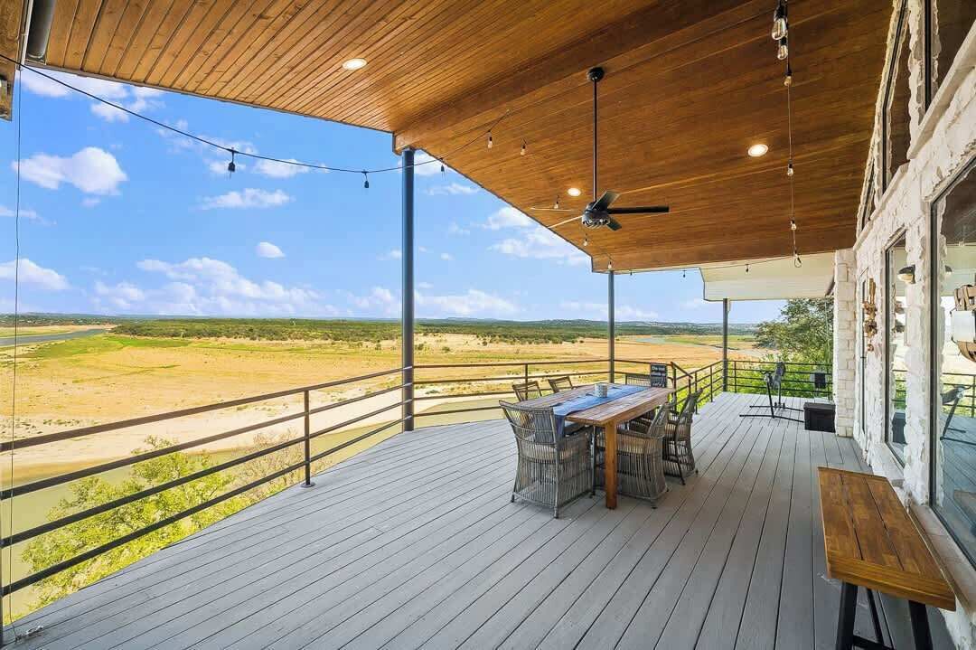 Een overdekt buitengebied met een houten terras, een tafel met stoelen en uitzicht op een landschap.