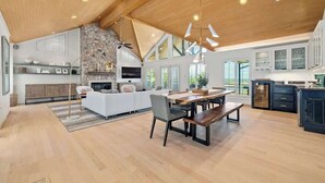 Une cuisine spacieuse équipée d’appareils modernes, un coin repas avec une table et des bancs en bois, et un salon confortable avec une cheminée.