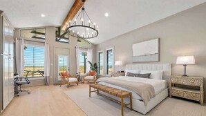Une chambre spacieuse avec un grand lit, un banc en bois, deux chaises, un bureau et une table de chevet.