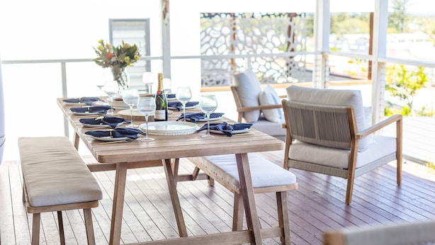 Une terrasse en bois avec une table à manger pour quatre personnes, entourée de chaises rembourrées.