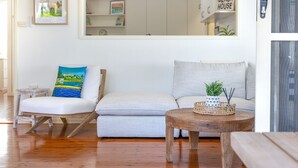 Un salon doté d’un plancher en bois, d’un canapé blanc, d’un fauteuil à bascule en bois et d’une petite table sur laquelle sont posés une plante et des bougies.