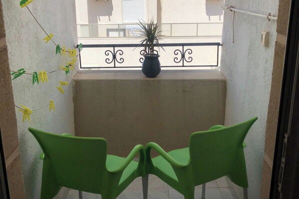A small balcony with a potted plant, two green chairs, and a decorative string of yellow and green paper flowers.