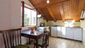 A cozy kitchen with wooden beams, a dining table with chairs, and a window with a view of greenery.