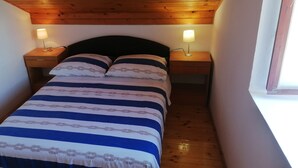 A narrow room with a bed, two bedside tables with lamps, wooden ceiling, and a window.