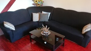 A black sofa with striped and solid pillows, a glass coffee table with a decorative centerpiece, and a red wooden floor.