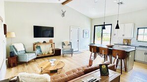 A spacious living room with a large sofa, a coffee table, and a television. There is a kitchen area with a dining table and chairs. - Modern Farmhouse w/Privacy, Views and Hot Tub! (GRAND JUNCTION)