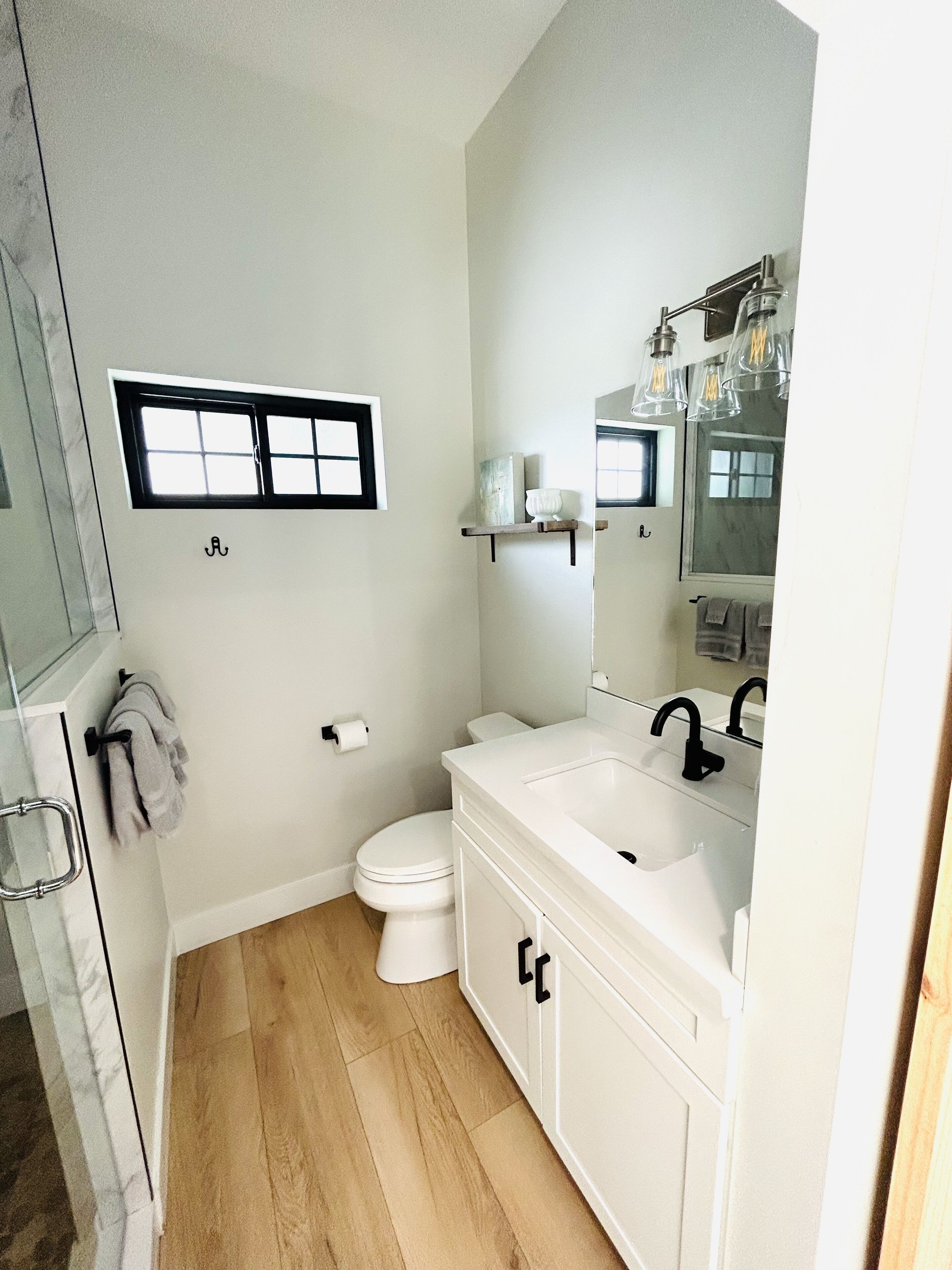 A bathroom with a toilet, sink, mirror, and a window.