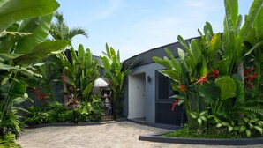 A modern building with a paved entrance surrounded by lush tropical plants and a clear blue sky. - Je Ne Sais Quoi Seminyak (Seminyak)