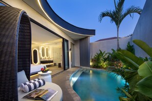 A modern outdoor pool area with a curved wall, a lounge chair, and a small table with a fruit bowl. - Je Ne Sais Quoi Seminyak (Seminyak)