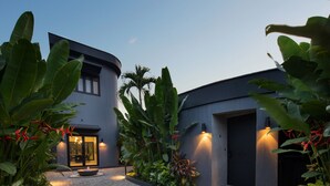 A modern building with a curved facade, a paved courtyard, and lush tropical plants. - Je Ne Sais Quoi Seminyak (Seminyak)