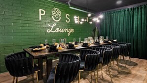 Ein Essbereich mit einem langen Tisch, gedeckt für eine Mahlzeit, grünen Ziegelwänden und einem Schild mit der Aufschrift "POS Lounge".