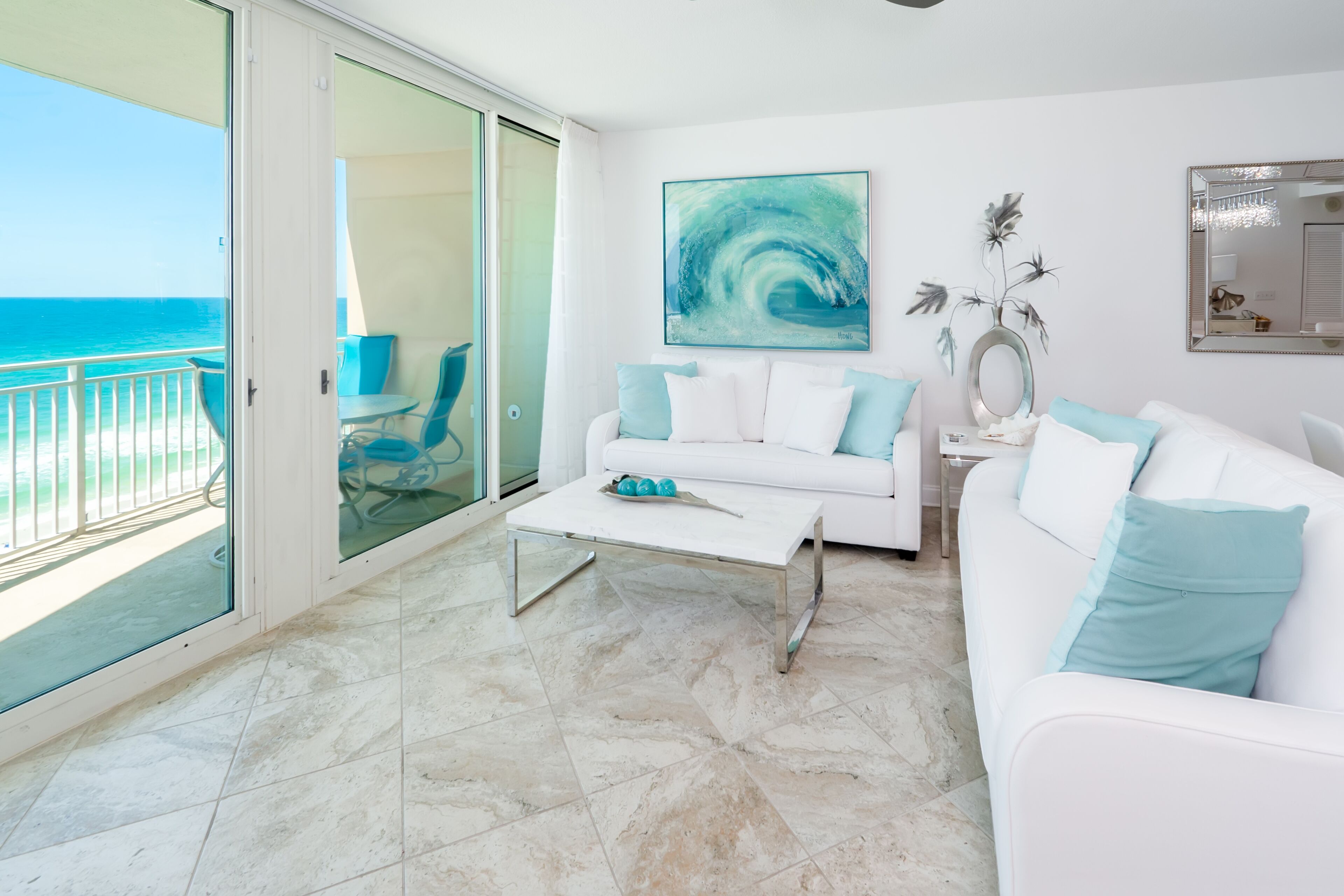 A modern living room with a white sofa, a coffee table, and a painting of a wave.