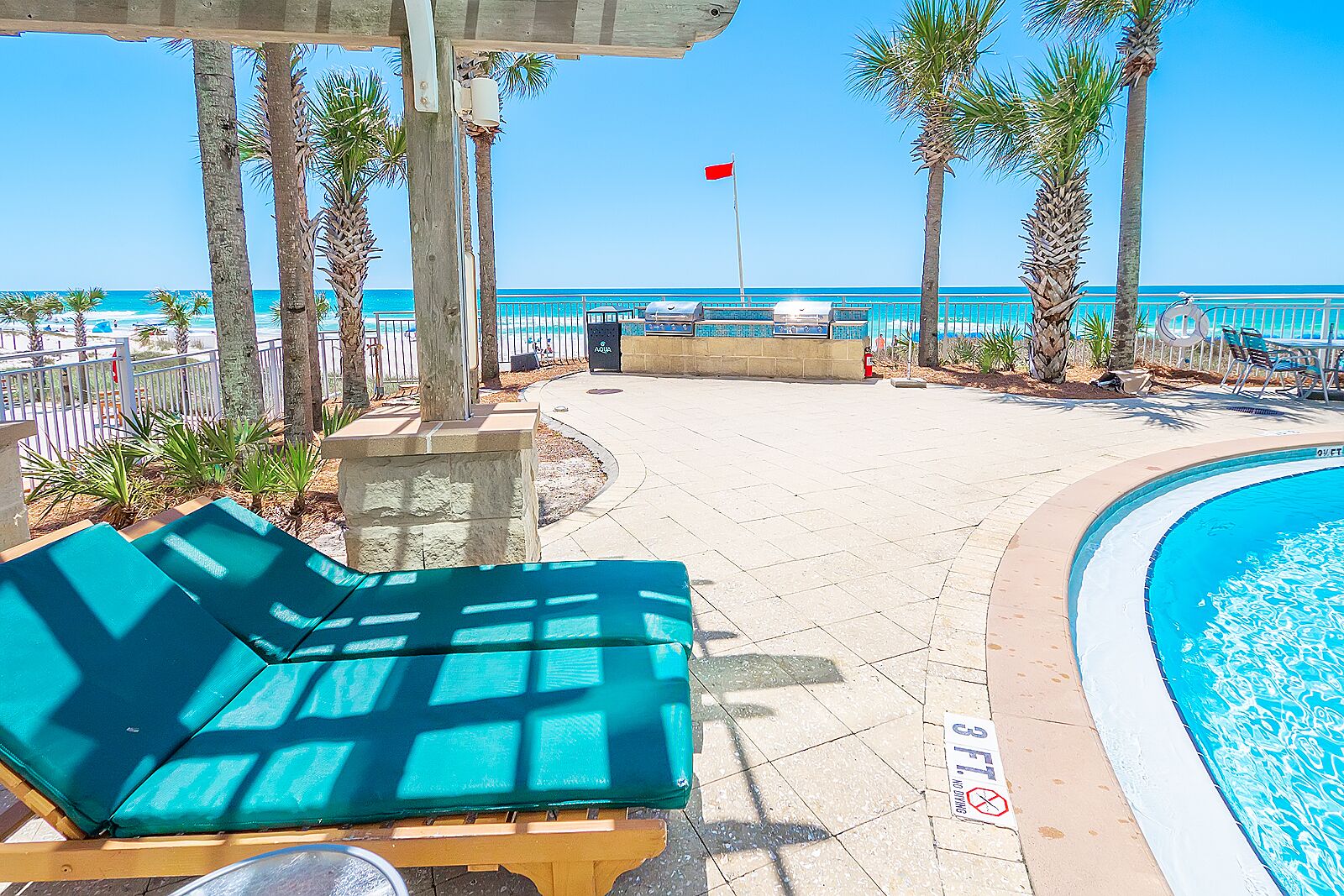 A poolside area with lounge chairs, a pool, and a view of the ocean.