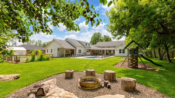 A large house with a swimming pool, surrounded by a well-maintained lawn and trees.