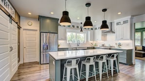 A modern kitchen with a large island, bar stools, and pendant lighting.