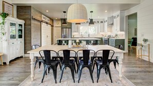 A spacious kitchen with a large island, black chairs, and pendant lighting.