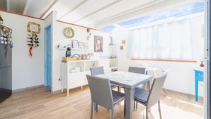 Una stanza luminosa con un tavolo da pranzo, sedie, un frigorifero e una finestra con tende.