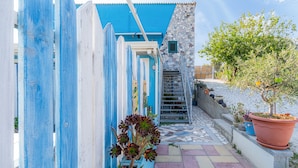 Un stretto vicolo con un recinto dipinto di blu e bianco, un muro in pietra e un percorso piastrellato che conduce a una scala.