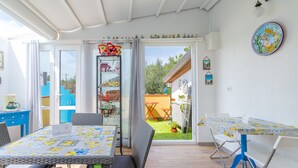 Zona pranzo con tavolo e sedie, angolo cottura con pensili e frigorifero, e una porta scorrevole in vetro che dà su un giardino.