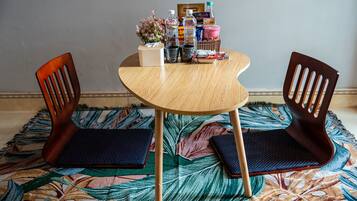 A round wooden table with two chairs, a patterned rug, and various items on the table including a tissue box, a bottle, and snacks.