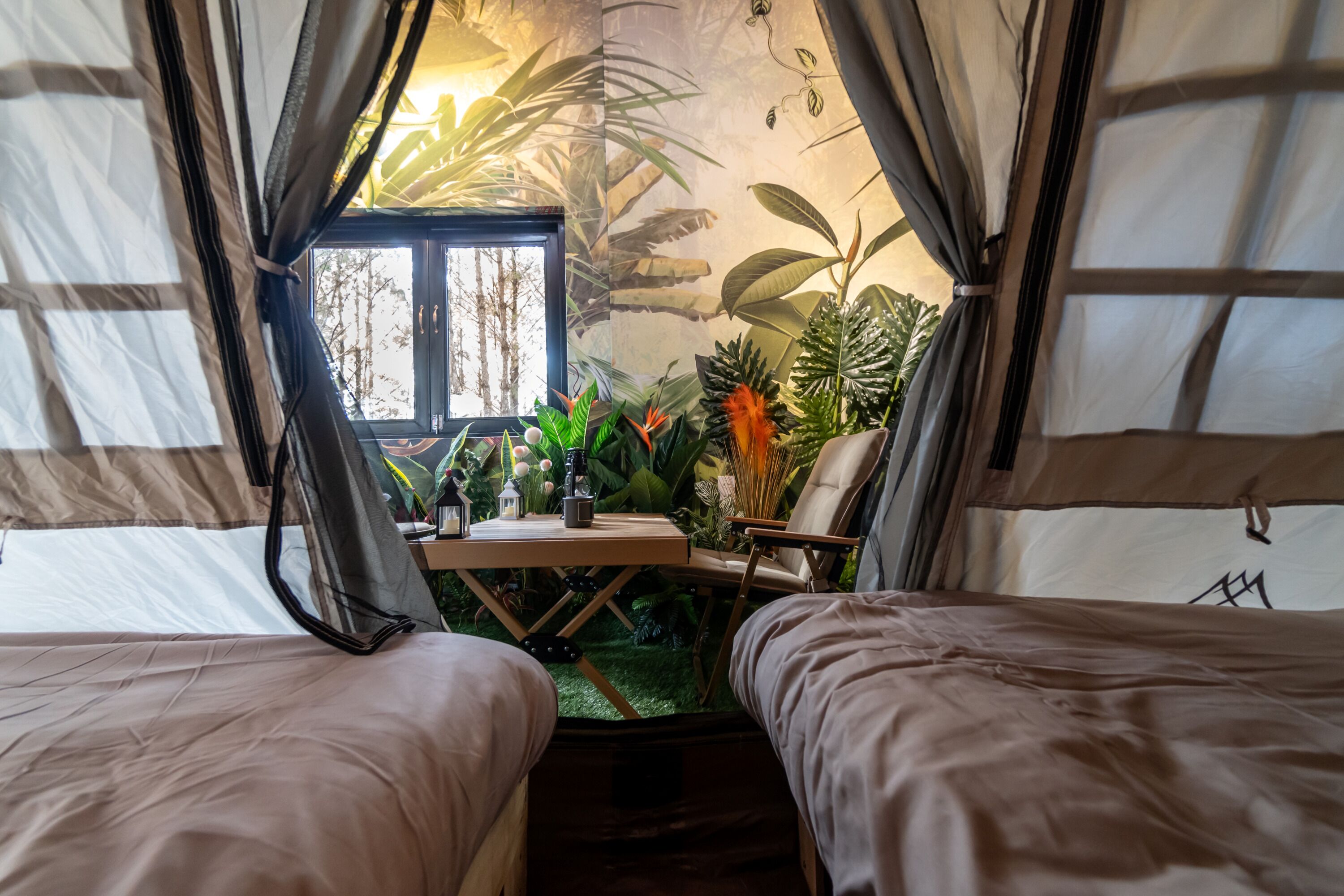 Una carpa con dos camas, una mesa con una lámpara y vistas a árboles a través de una ventana.