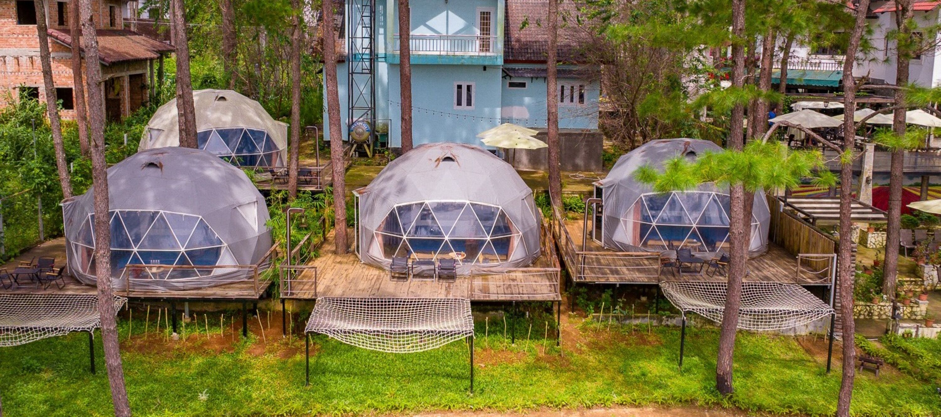 Geodesic dome structures with mesh floors, surrounded by trees and a small water body.