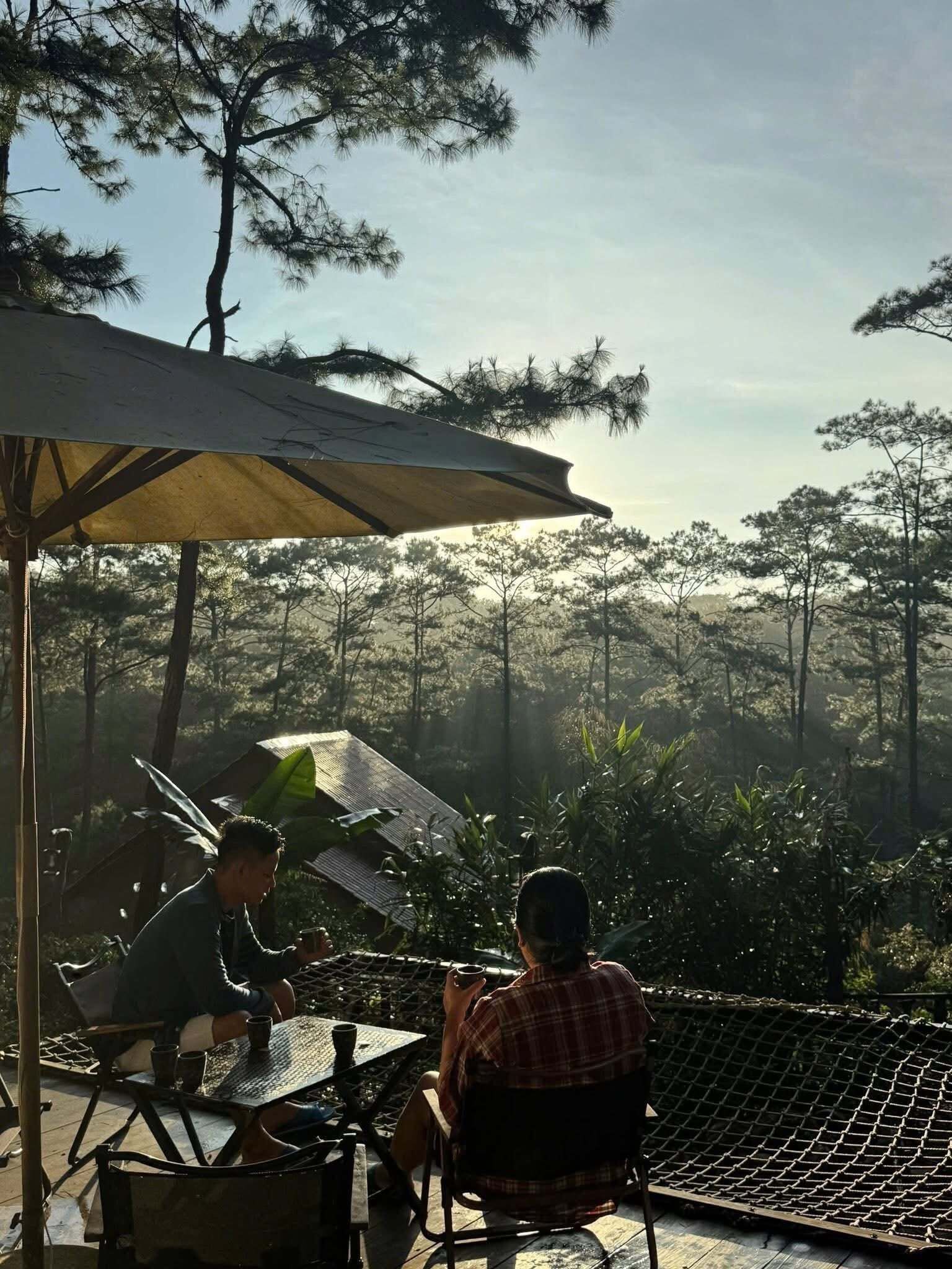 An outdoor seating area with a table and chairs, surrounded by a netted enclosure, overlooking a forested landscape.