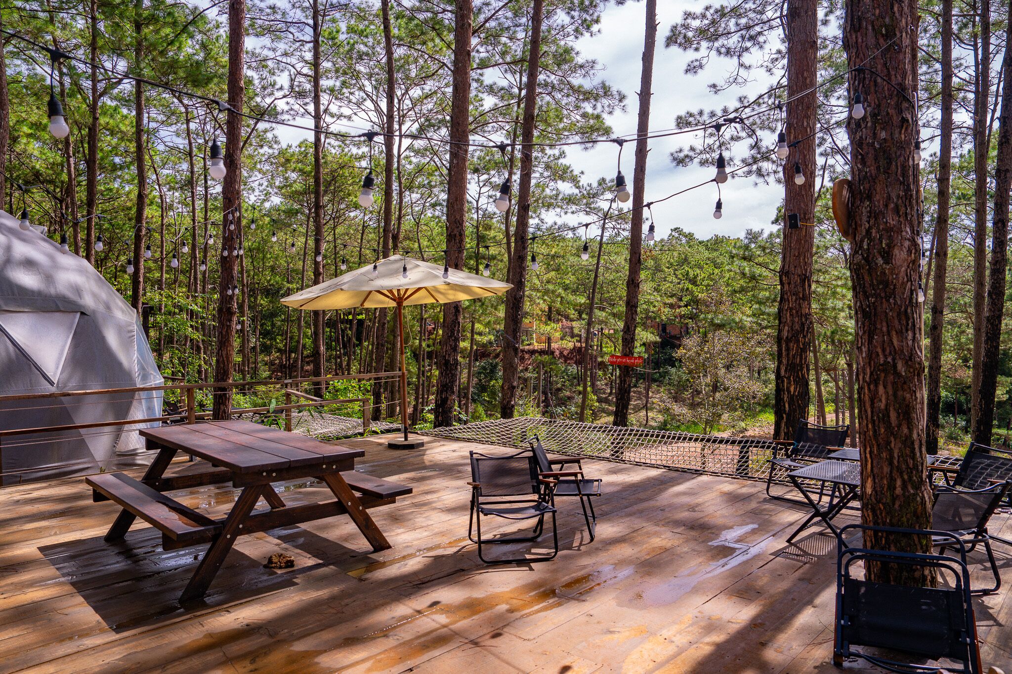 A wooden deck with picnic tables and chairs, surrounded by trees and a tent.