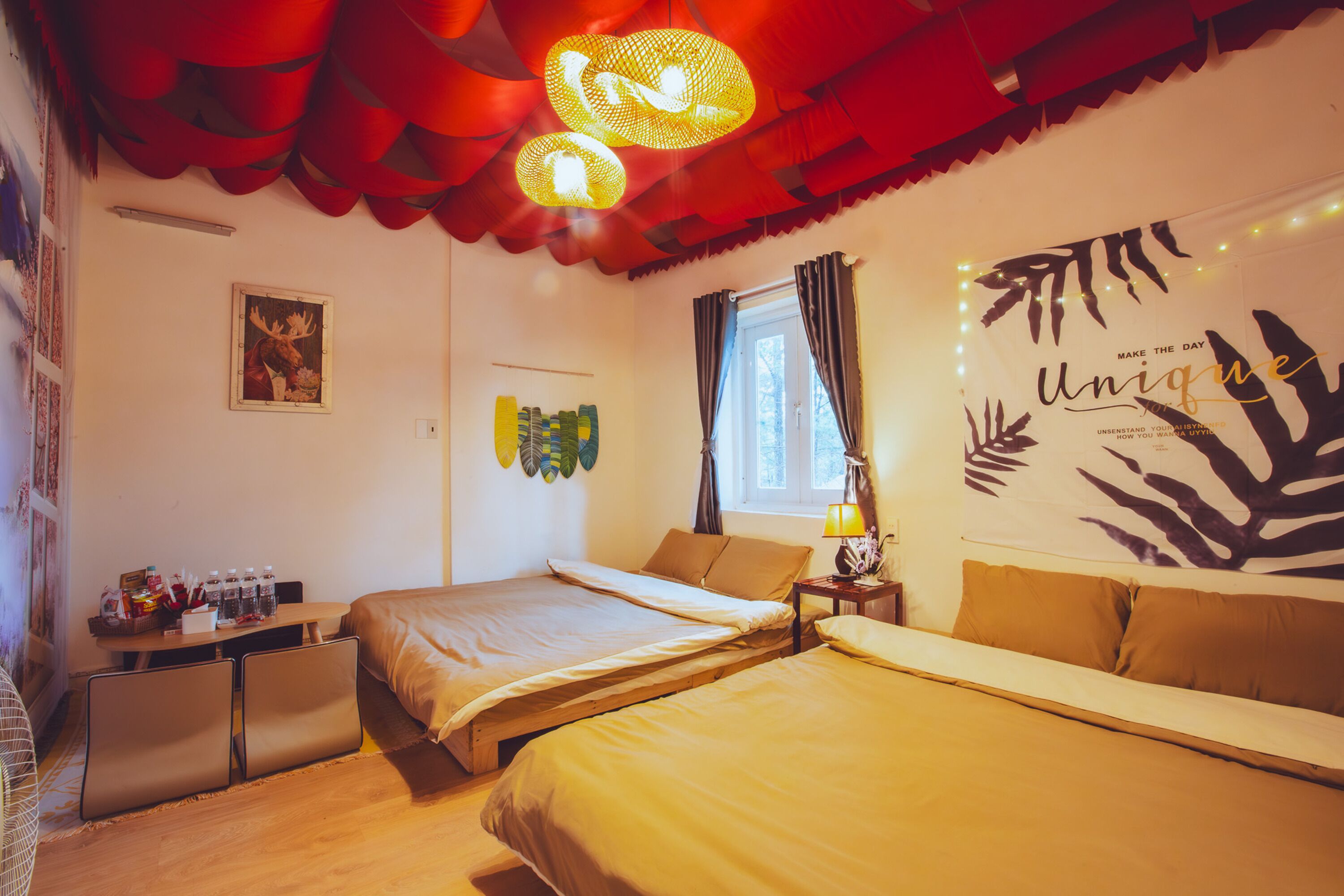 A hotel room with two beds, a desk, a chair, a window with curtains, and wall art.