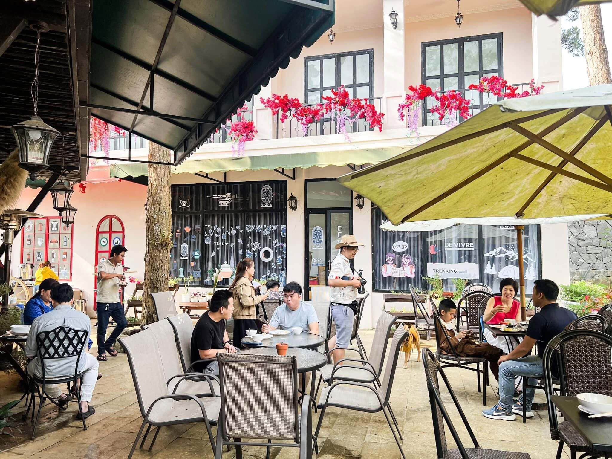 An outdoor cafe with tables and chairs, a covered seating area, and a building with a balcony decorated with flowers.