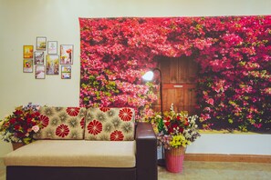 Een kamer met een bank, een groot wandtapijt met rode bloemen, en een muur met ingelijste foto's.