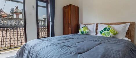 A bedroom with a large bed, a wooden wardrobe, and a balcony with a view of traditional architecture.
