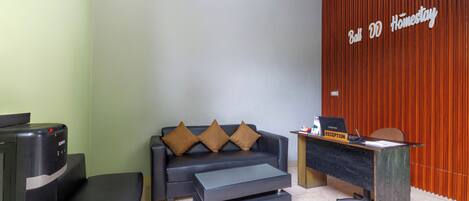 Ein Empfangsbereich mit einer Rezeption, einer Couch mit Kissen, einem Couchtisch und einem Verkaufsautomaten.