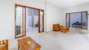 Um quarto espaçoso com uma mesa de madeira, um banco e uma cama. Há portas de vidro deslizantes que levam a outro quarto.
