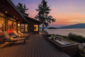 Un pontile in legno con poltrone relax e una sala con vetrate affacciata sull'acqua.